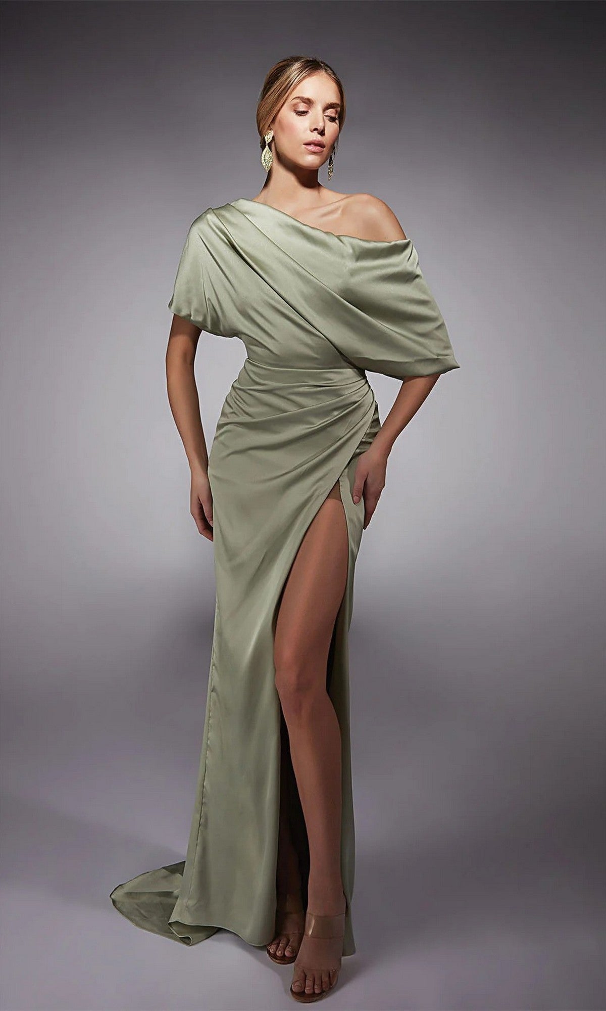 A woman in the Alyce 27748 long formal dress in celadon, featuring an off-the-shoulder satin design with a ruched bodice and high-leg side slit, stands against a plain gray background.